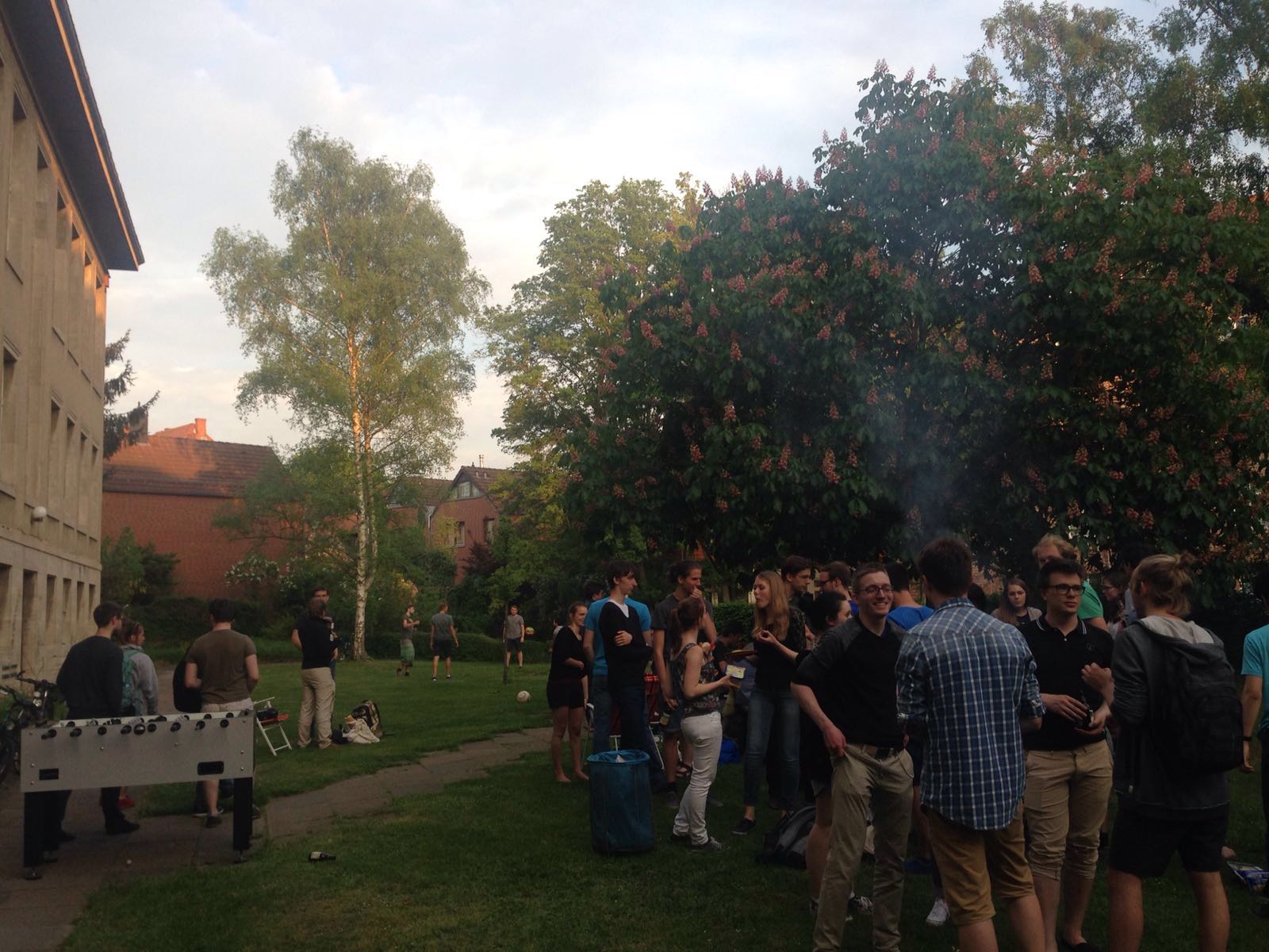 Mathe-Info-Stammtisch im Mathegarten. Ein paar Leute spielen Ball, andere stehen um einen Grill und reden